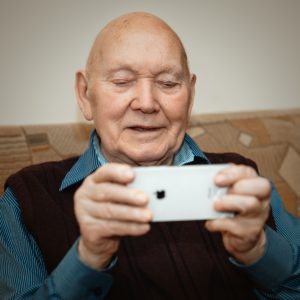 old man in blue and black pinstripe dress shirt holding white smartphone